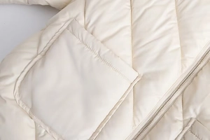 Detail of beige quilted jacket featuring a large square pocket and metallic zipper closure
