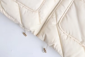 Detail of diamond quilted pattern on cream jacket with golden zipper and drawstring