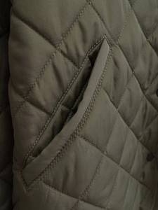 Détail d'une veste matelassée vert olive avec surpiqûres en losanges et poche à bouton