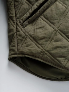 Detail of olive green quilted jacket featuring diamond stitching and curved hemline