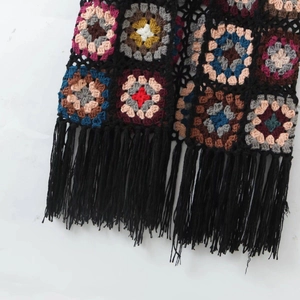 Detailed close-up of handmade crochet granny squares with long black fringe tassels