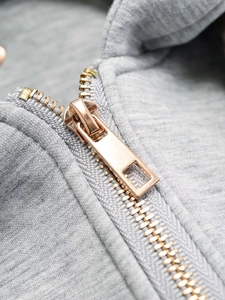 Detail of light gold metal zipper on grey quilted jacket with knit cotton texture