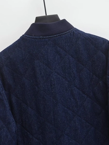 Detail of navy blue quilted denim jacket featuring a ribbed stand collar and diamond stitching
