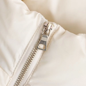 Detailed close-up of a silver polished metal zipper on a cream quilted winter jacket