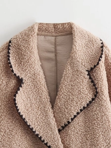 Détail du col à revers avec surpiqûres noires sur veste beige en peau lainée