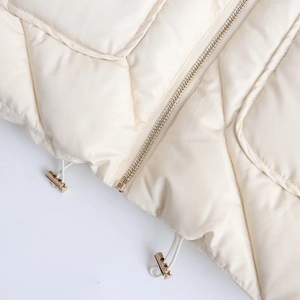 Detailed close-up of cream quilted cotton jacket showing metal zipper and elastic drawstring