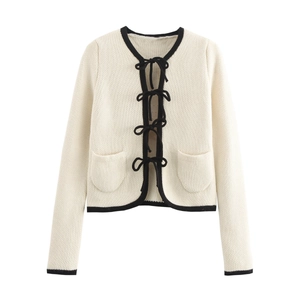 Detail of cream knit cardigan featuring black contrast edges and bow-tie front ribbon closures