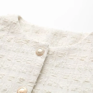 Détails du tissu en tweed texturé et boutons en métal doré sur une veste de couleur crème