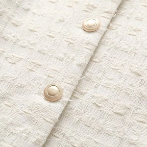 Vue détaillée de la texture en tweed blanc et des boutons décoratifs en métal doré