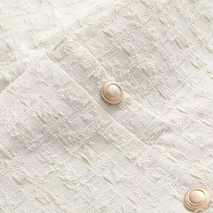 Vue macro du tissu en tweed crème et des boutons en métal doré texturé sur le cardigan