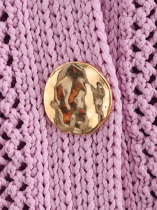Macro detail of textured gold hammer-tone button on pink crochet knit cardigan