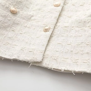 Gros plan sur une veste en tweed blanc avec boutons dorés et ourlet à bord brut chic