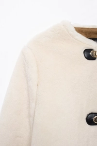 Detailed macro view of cream faux fur jacket with gold metal buckle and leather trim