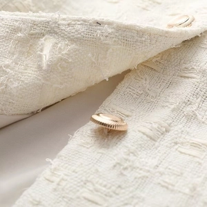 Détail de la veste en tweed crème avec boutons dorés en relief et tissu tissé