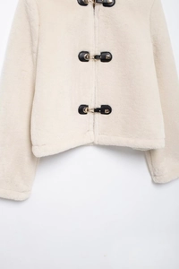 Detailed close-up of faux fur jacket with black leather trim and golden metal buckles