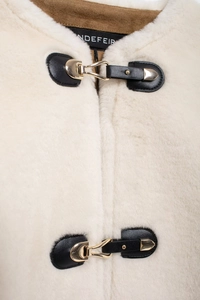Detail of cream faux fur jacket featuring black leather patches and gold metal buckles