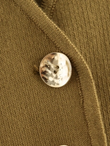 Close-up of a vintage golden hammered button on a dark yellow knit vest with ribbed edges