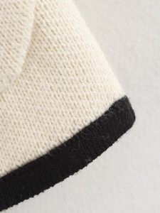 Close-up of cream chunky knit cardigan sleeve with black trim detail and soft texture