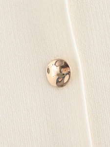Détail d'un bouton métallique doré et d'une texture en tricot crème sur le haut