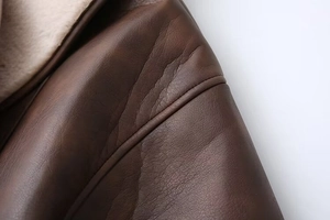 Detail of dark brown leather jacket with soft cream-white shearling lining and stitching