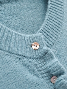 Close-up of soft light blue knit cardigan featuring ruffled crew neck and pearl buttons