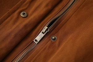 Détail macro de la fermeture éclair et des boutons-pression sur la veste caramel