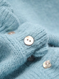 Close-up of soft light blue knit sweater featuring shiny pearl buttons and fuzzy texture