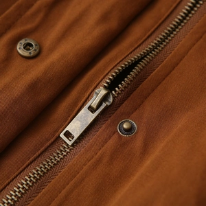 Détail des boutons en laiton avec étoiles et fermeture éclair sur veste en toile marron