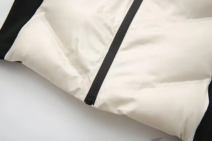 Détail du gilet matelassé blanc avec fermeture éclair noire et panneaux latéraux côtelés