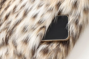 Detail showing the elegant gold metallic edge of the phone case against fluffy leopard fur
