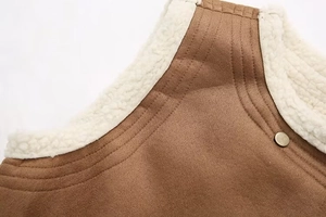 Detail of brown suede vest featuring white faux shearling lining and bronze metal snap button