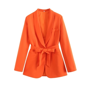 Detail of vibrant orange blazer with shawl lapel and belt tied in a bow over flap pockets
