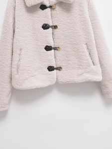 Detail of faux fur cropped jacket with black leather buckles and gold metal fasteners