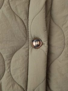 Gros plan sur la veste matelassée olive avec coutures ondulées et bouton en écaille