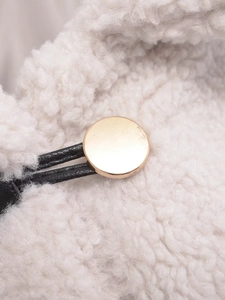 Detailed close-up of premium white faux lamb wool texture with gold metal fastener