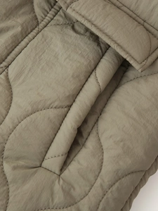 Détail macro d'une veste matelassée vert olive montrant les coutures et la poche