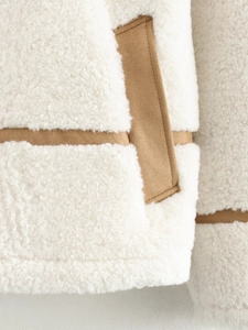 Detail of white sherpa jacket featuring brown suede trim and pocket stitching design