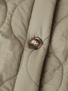 Gros plan sur la texture matelassée ondulée et le bouton en résine d'une veste coton