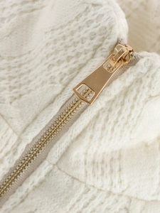 Detail of chunky knit fabric texture and polished gold zipper on the beige cardigan