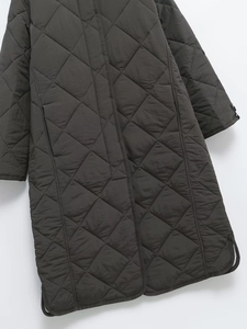 Detail view of diamond-quilted texture and side slit hem on a long quilted coat