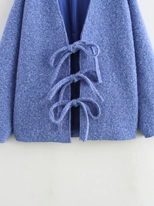 Dettaglio del tessuto bouclé blu reale e chiusura con fiocchi eleganti su un cappotto