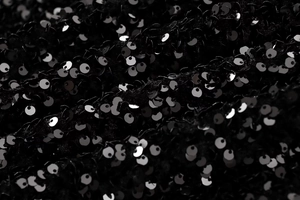 Macro shot of black sequin fabric texture with reflective metallic circular disks
