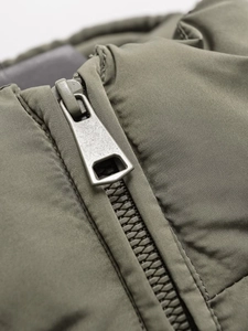 Detailed close-up of heavy-duty metal zipper and quilted texture on olive puffer jacket