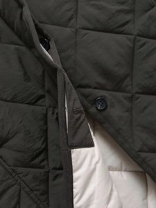 Detailed close-up of olive green quilted jacket with diamond patterns and black buttons