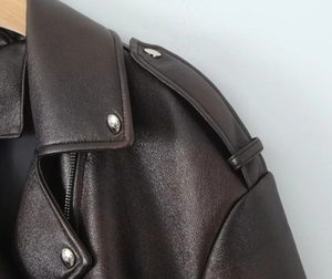 Gros plan d'une veste en cuir grainé marron foncé avec fermetures éclair et boutons argentés