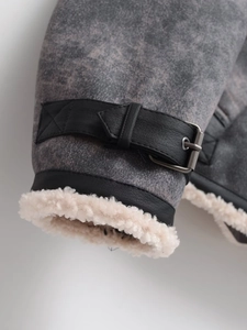 Macro view of jacket cuff with distressed grey fabric, leather strap and faux shearling lining