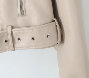 Détail de la veste en cuir PU crème avec œillets métalliques argentés et texture ceinture