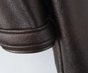 Vue détaillée de la texture du cuir PU marron foncé et des surpiqûres de la veste