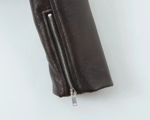 Détail d'une manche de veste en similicuir marron foncé avec une fermeture éclair argentée