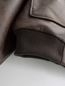 Macro detail of dark brown faux leather texture and ribbed knit cuff on bomber jacket